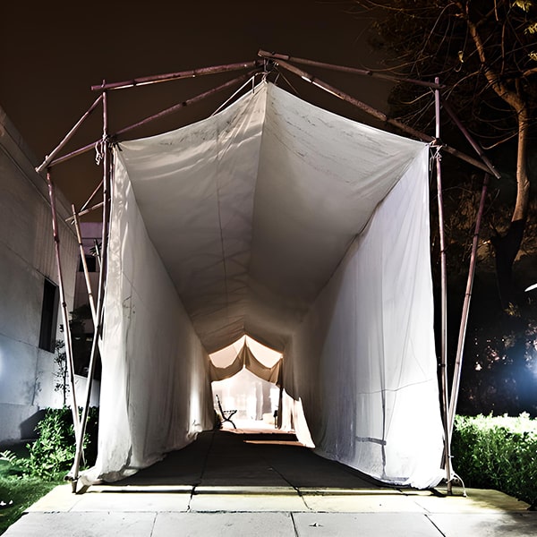 This temporary structure, made of repurposed bamboo, canvas and cotton rope, served as the entry to a music/art/food festival. The task was to create a tunnel using a supply of used, precut bamboo which could be quickly and easily built. The structure is a simple and elegant 3-pinned bamboo arch module, with cotton rope tensile cross-bracing. The canvas walls, sewn and then tied to the interior of the archway, create a blank screen onto which is projected an undulating animation of light, which draws the visitor through the tunnel and into the festival space. Delhi, India, 2011